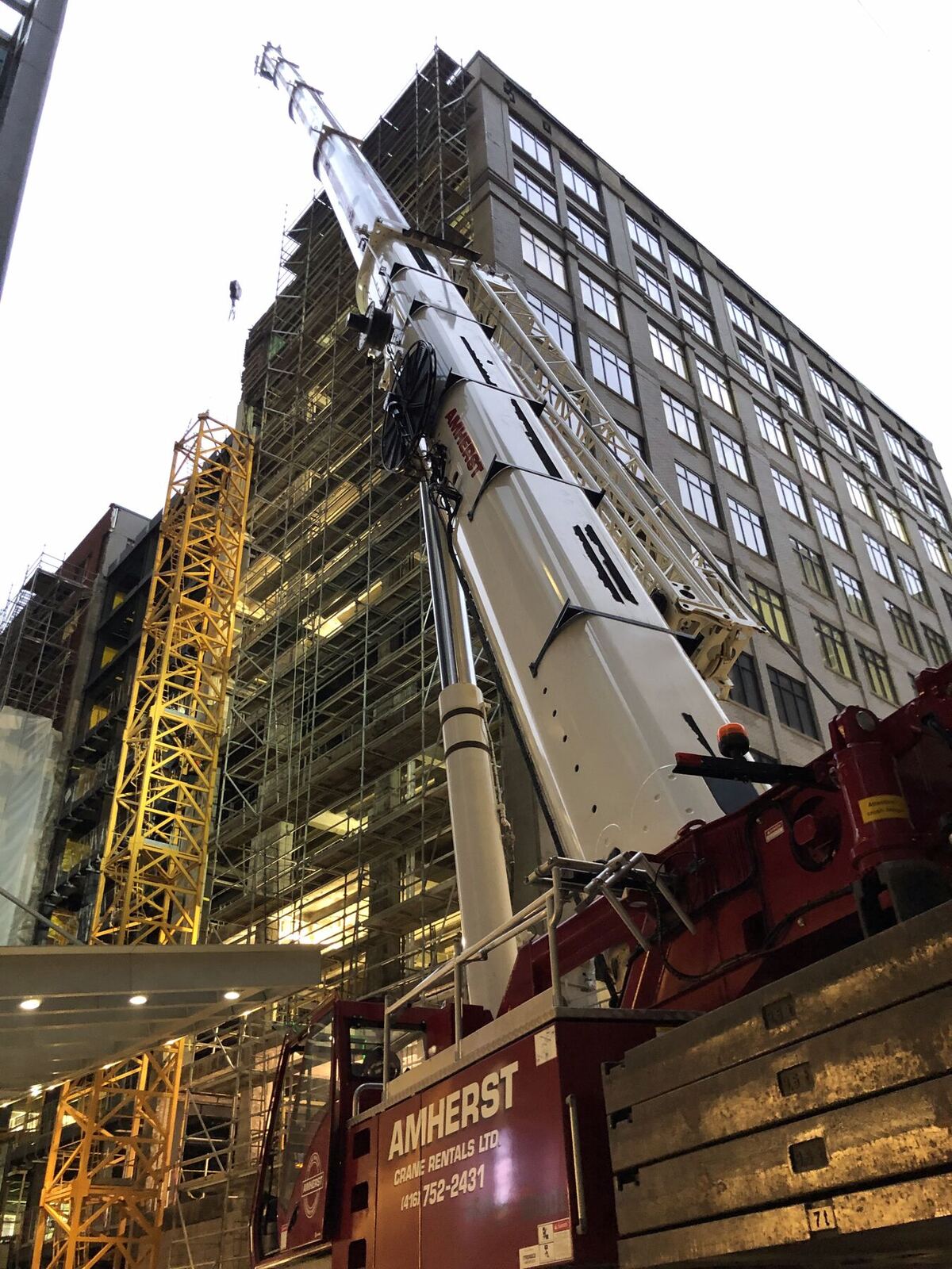 Mobile crane boom raised beside a scaffolded mid-rise building on a tight urban street